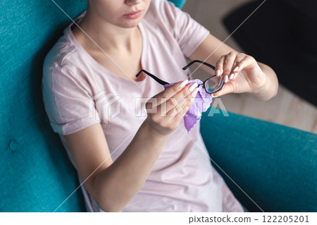 Young woman cleaning glasses with a napkin while sitting in a ch 122205201