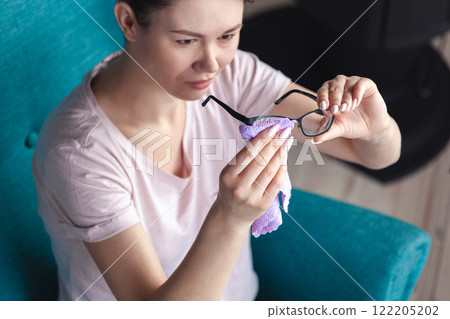 Young woman cleaning glasses with a napkin while sitting in a ch Young woman cleaning glasses with a napkin while sitting in a ch 122205202