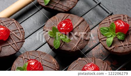 Chocolate brownies beautifully topped with bright red cherries and fresh mint leaves, placed on a cooling rack for an elegant presentation. Chocolate brownies beautifully topped with bright red cherries and fresh mint leaves, placed on a cooling rack for an elegant presentation. 122206279