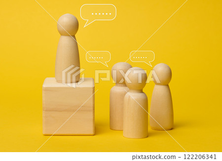 Wooden figures on a yellow background symbolize communication and leadership, one figure stands on a pedestal Wooden figures on a yellow background symbolize communication and leadership, one figure stands on a pedestal 122206341