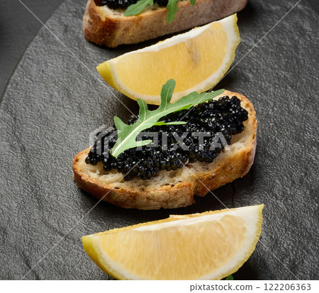 Sandwiches with black sturgeon caviar on a black plate and lemon slices Sandwiches with black sturgeon caviar on a black plate and lemon slices 122206363