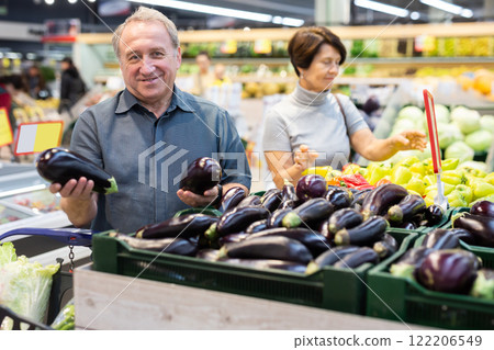 Elderly man chooses eggplants in vegetable and fruit department Elderly man chooses eggplants in vegetable and fruit department 122206549