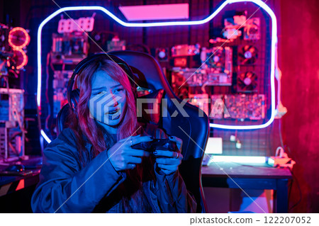 Woman wear gaming headphones playing esports games console gaming room, Gamer using joystick controller for race tournament plays online video game with computer neon lights Woman wear gaming headphones playing esports games console gaming room, Gamer using joystick controller for race tournament plays online video game with computer neon lights 122207052