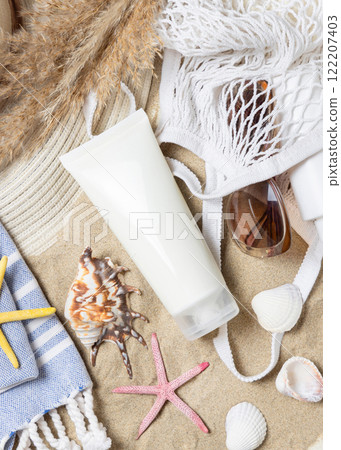 Sunscreen cream tube, sunglasses, towel, starfishes and seashells on a sand, cosmetic mockup 122207403