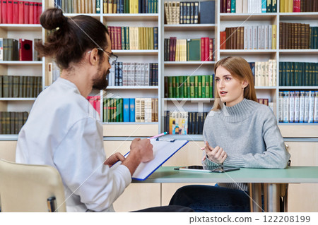 Teenage student girl talking with male teacher, social worker, school counselor in library Teenage student girl talking with male teacher, social worker, school counselor in library 122208199
