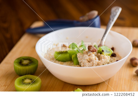 cooked oatmeal with kiwi, honey and nuts in a bowl on a wooden table 122208452