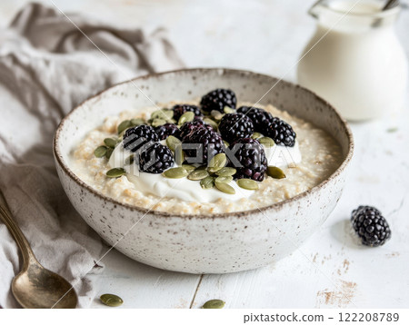 Creamy bowl of porridge topped with fresh blackberries and seeds, perfect for breakfast 122208789