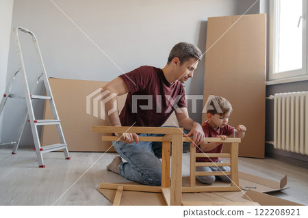 Smiling dad teaches his little son how to use tools while assembling furniture together Smiling dad teaches his little son how to use tools while assembling furniture together 122208921