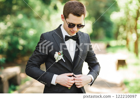 Happy handsome smiling groom posing with boutonniere Happy handsome smiling groom posing with boutonniere 122210097