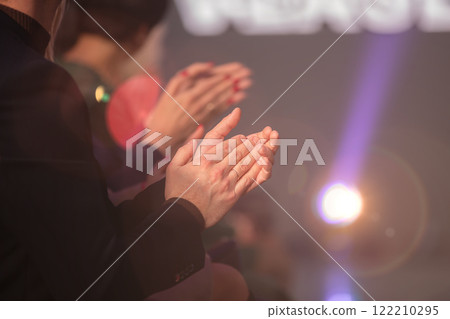 Applause. The audience's hands clap against the background of the stage lighting. Applause. The audience's hands clap against the background of the stage lighting. 122210295