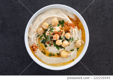 Chickpea hummus with olive oil, parsley and paprika in bowl on black background 122210343