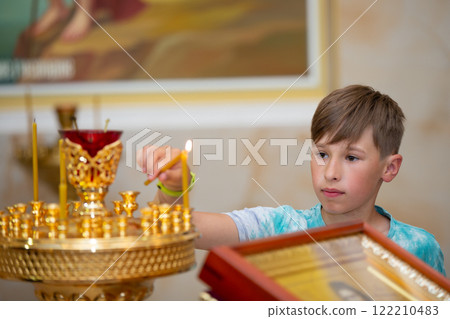 A teenage boy puts candles in an Orthodox church . A teenage boy puts candles in an Orthodox church . 122210483