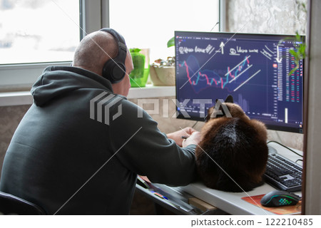 A male trader sits at home at a computer, monitors the schedule on the stock exchange, is engaged in trading and stock trading. 122210485