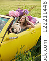 A young girl is sitting in a yellow convertible surrounded by bright flowers 122211448