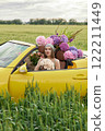 A young girl is sitting in a yellow convertible surrounded by bright flowers 122211449