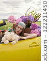 A young girl is sitting in a yellow convertible surrounded by bright flowers 122211450