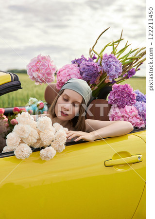A young girl is sitting in a yellow convertible surrounded by bright flowers 122211450