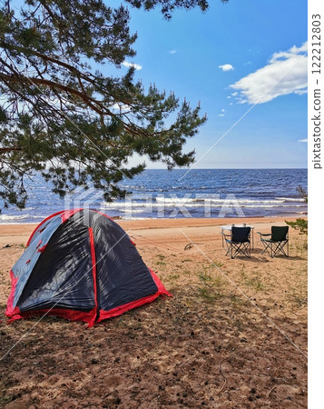 Camping beside the tranquil lake at sunset with a tent and chairs on the sandy beach 122212803
