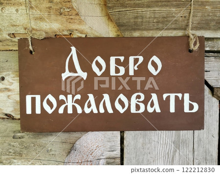 Welcome sign in Russian language hanging on rustic wooden wall, welcoming visitors to a cozy retreat 122212830