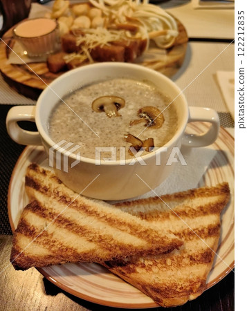 Delicious bowl of creamy mushroom soup with toasted bread served at a cozy restaurant in the evening 122212835