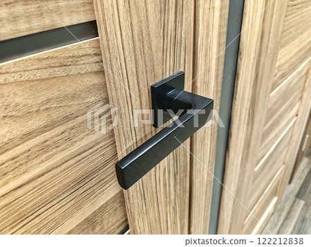 Modern black door handle on a wooden cabinet showcasing sleek design in a contemporary interior setting 122212838