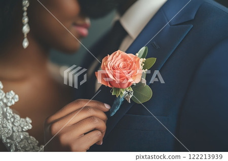 Bride gently adjusting a peach rose boutonniere on the groom's blue suit. A close-up of a tender wedding moment showcasing floral elegance and romantic attention to detail Bride gently adjusting a peach rose boutonniere on the groom's blue suit. A close-up of a tender wedding moment showcasing floral elegance and romantic attention to detail 122213939