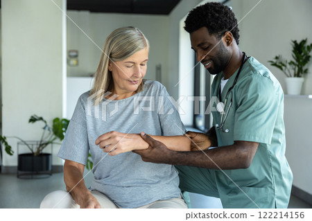 African American male doctor hand doing physical therapy by extending elbow of mature female patient 122214156