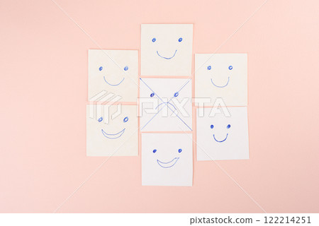 Crossed out sad face surrounded by happy smileys on paper cards on pink background. 122214251