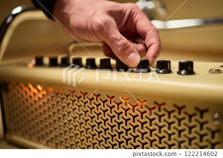 A musician is adjusting the amplifier settings for optimal sound quality during a performance A musician is adjusting the amplifier settings for optimal sound quality during a performance 122214602