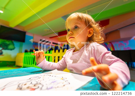 A cheerful child exploring creativity through coloring in a lively indoor playground. 122214736
