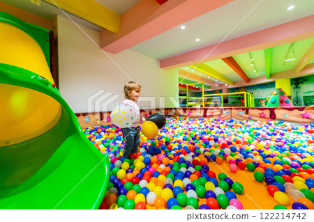 A child holding balloons surrounded by colorful balls in a vibrant indoor playground. A child holding balloons surrounded by colorful balls in a vibrant indoor playground. 122214742