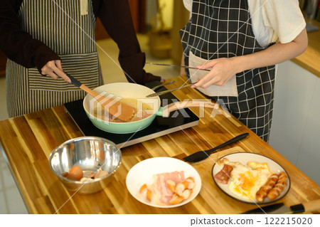Young male gay couple preparing a delicious breakfast at counter in warm kitchen Young male gay couple preparing a delicious breakfast at counter in warm kitchen 122215020