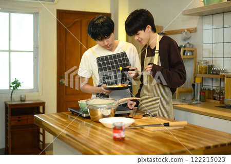 Young male gay couple preparing a delicious breakfast at counter in warm kitchen Young male gay couple preparing a delicious breakfast at counter in warm kitchen 122215023