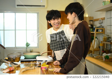 Happy gay couple in aprons preparing a delicious meal together in modern kitchen. Happy gay couple in aprons preparing a delicious meal together in modern kitchen. 122215040