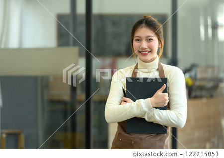 Confident and friendly coffee shop owner standing with clipboard in hand and smiling at the camera Confident and friendly coffee shop owner standing with clipboard in hand and smiling at the camera 122215051