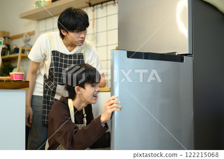 Young gay couple searching for ingredients in the fridge while preparing meal in their cozy kitchen 122215068