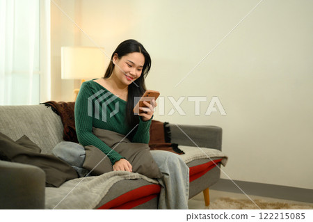 Pretty young woman in green sweater using her mobile phone on a cozy sofa 122215085