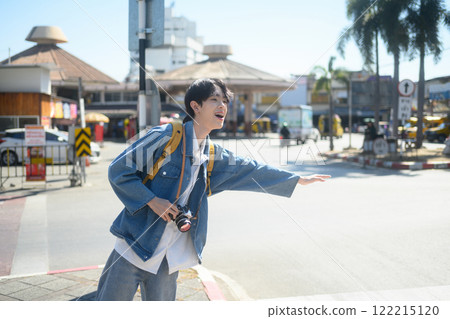 Smiling male traveler with a yellow backpack and camera hailing transportation in a city Smiling male traveler with a yellow backpack and camera hailing transportation in a city 122215120