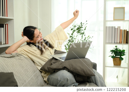 Relaxed young woman stretching on a couch taking a break during remote work Relaxed young woman stretching on a couch taking a break during remote work 122215208