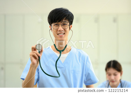 Confident medical student in blue scrubs holding up stethoscope, ready to practice patient care Confident medical student in blue scrubs holding up stethoscope, ready to practice patient care 122215214