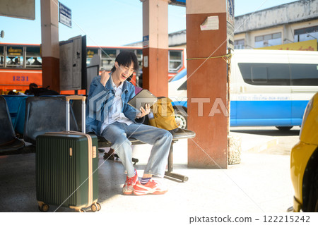 Excited traveler looking at digital tablet and celebrating sitting in a transportation terminal with a suitcase Excited traveler looking at digital tablet and celebrating sitting in a transportation terminal with a suitcase 122215242