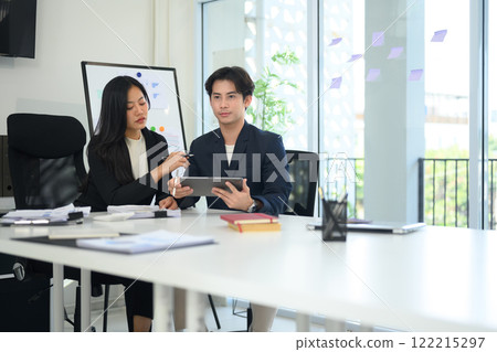 Shot of two businesspeople in formal suit working together in a modern office, reviewing data on digital tablet 122215297