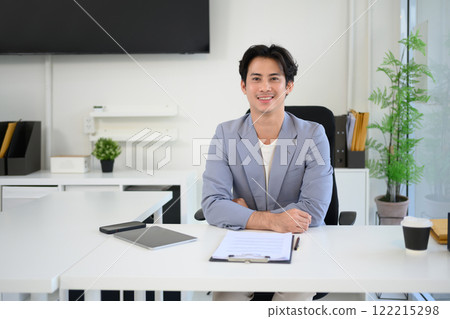 Portrait of confident businessman in stylish suit sitting at his desk with documents and digital tablet 122215298