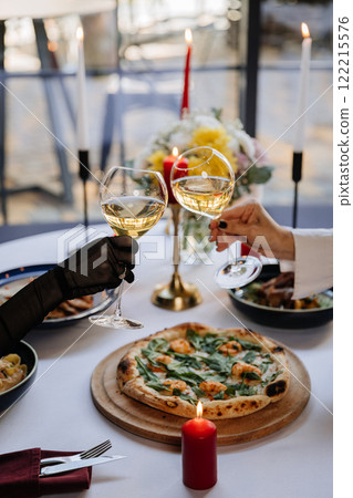 Elegant toast with white wine at a candlelit dinner, celebrating with gourmet pizza and fine dining 122215576