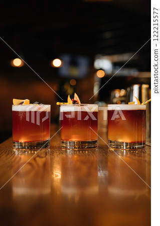 Three vibrant cocktails on a wooden bar counter, perfect for nightlife and mixology themes 122215577