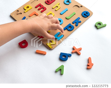 Childs hand arranging colorful alphabet puzzle on white background Childs hand arranging colorful alphabet puzzle on white background 122215773