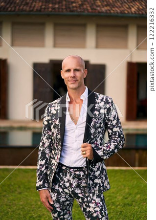 Bald man, floral suit, confident at luxury villa. Bold, stylish outfit, wedding, gay groom theme. High-end event, modern fashion, classy aesthetics. Perfect for wedding, fashion. 122216332