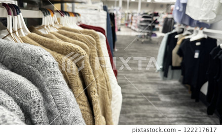 cozy knitted sweaters in shades of gray, beige, and red hanging on a clothing rack in a retail store 122217617