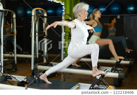 Senior woman standing on pilates reformer, perform exercises 122218406