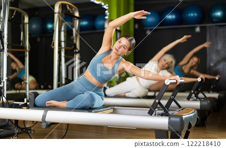 Girl sitting on foldable bed reformer performs exercises, strengthening body and muscles Girl sitting on foldable bed reformer performs exercises, strengthening body and muscles 122218410